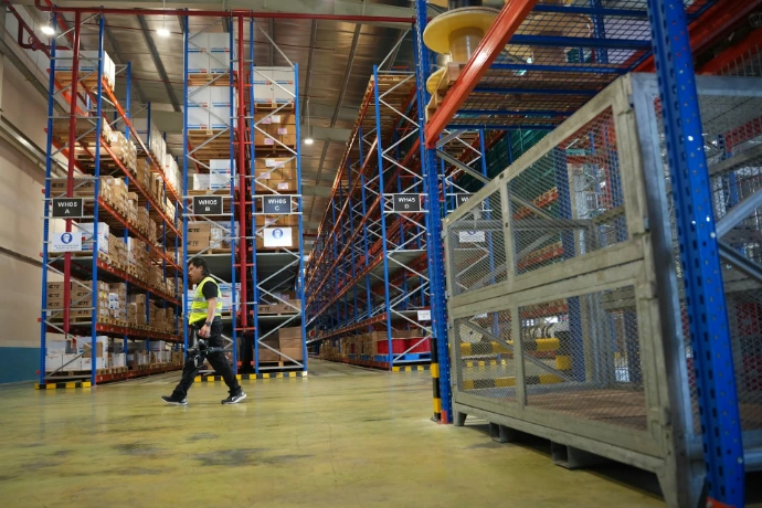 Man walks through a brightly lit warehouse with tall shelves.